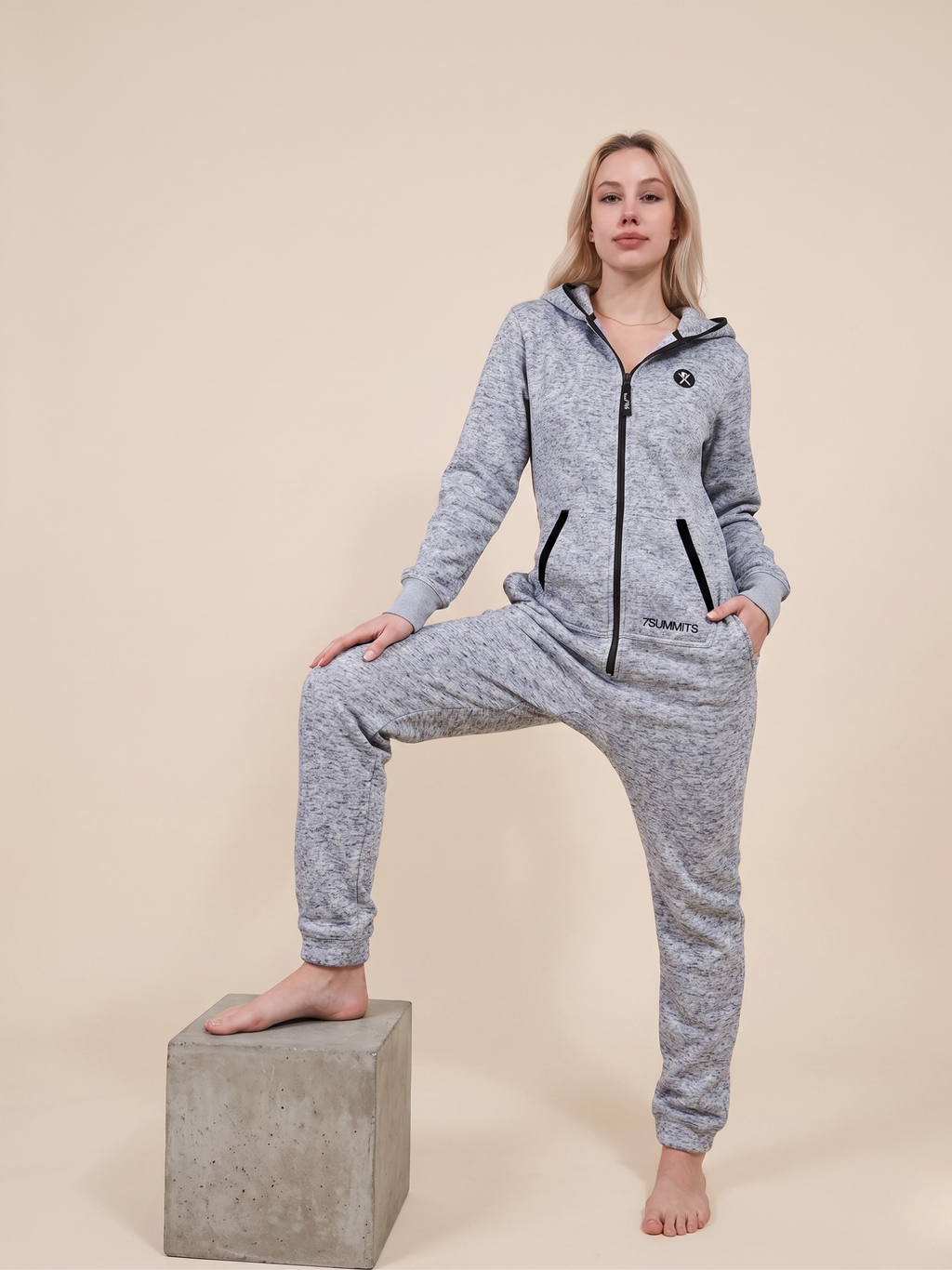 Person wearing a gray onesie with a brand logo on a beige background

