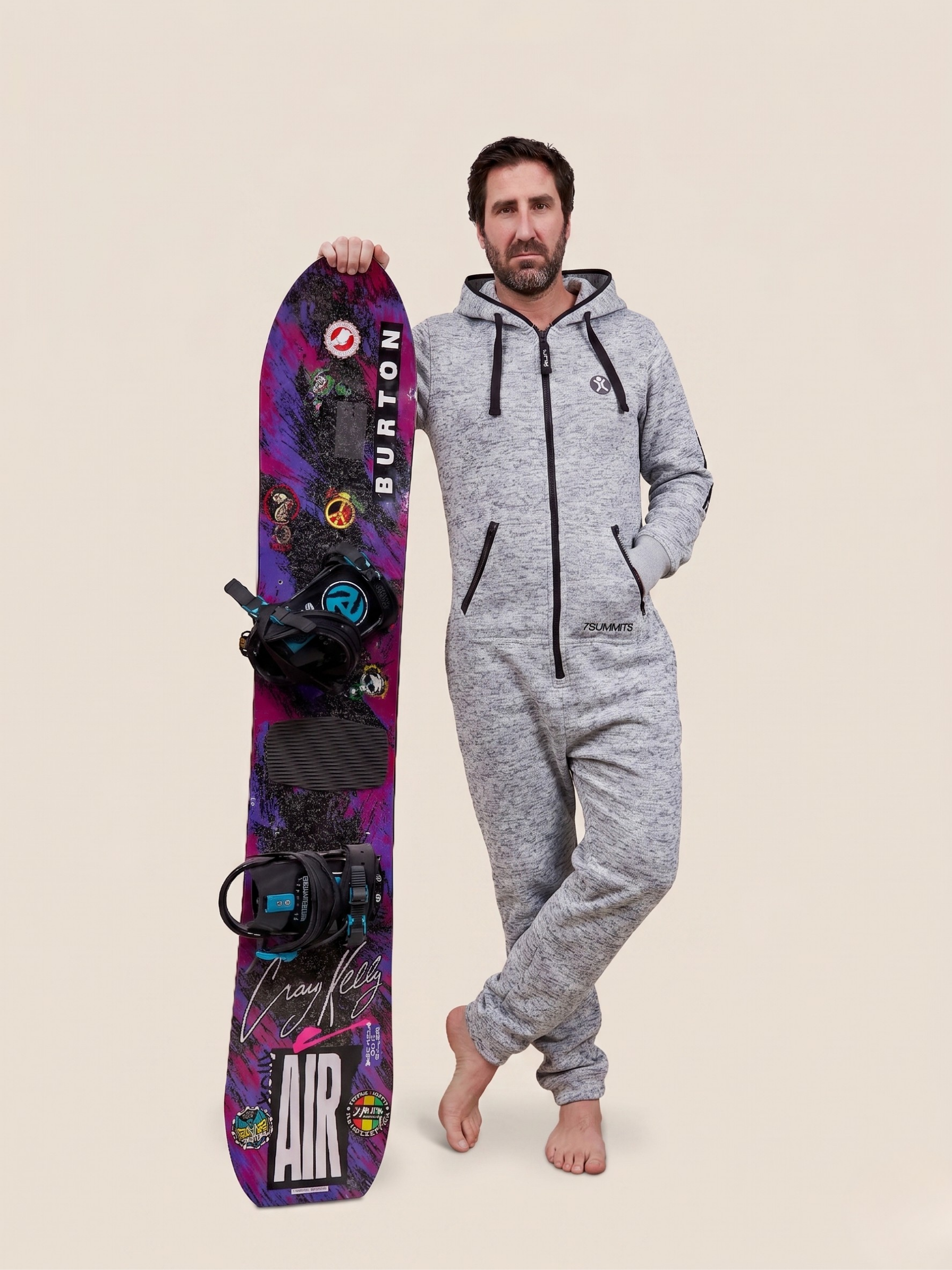 Man in a gray onesie holding a Burton snowboard against a beige background