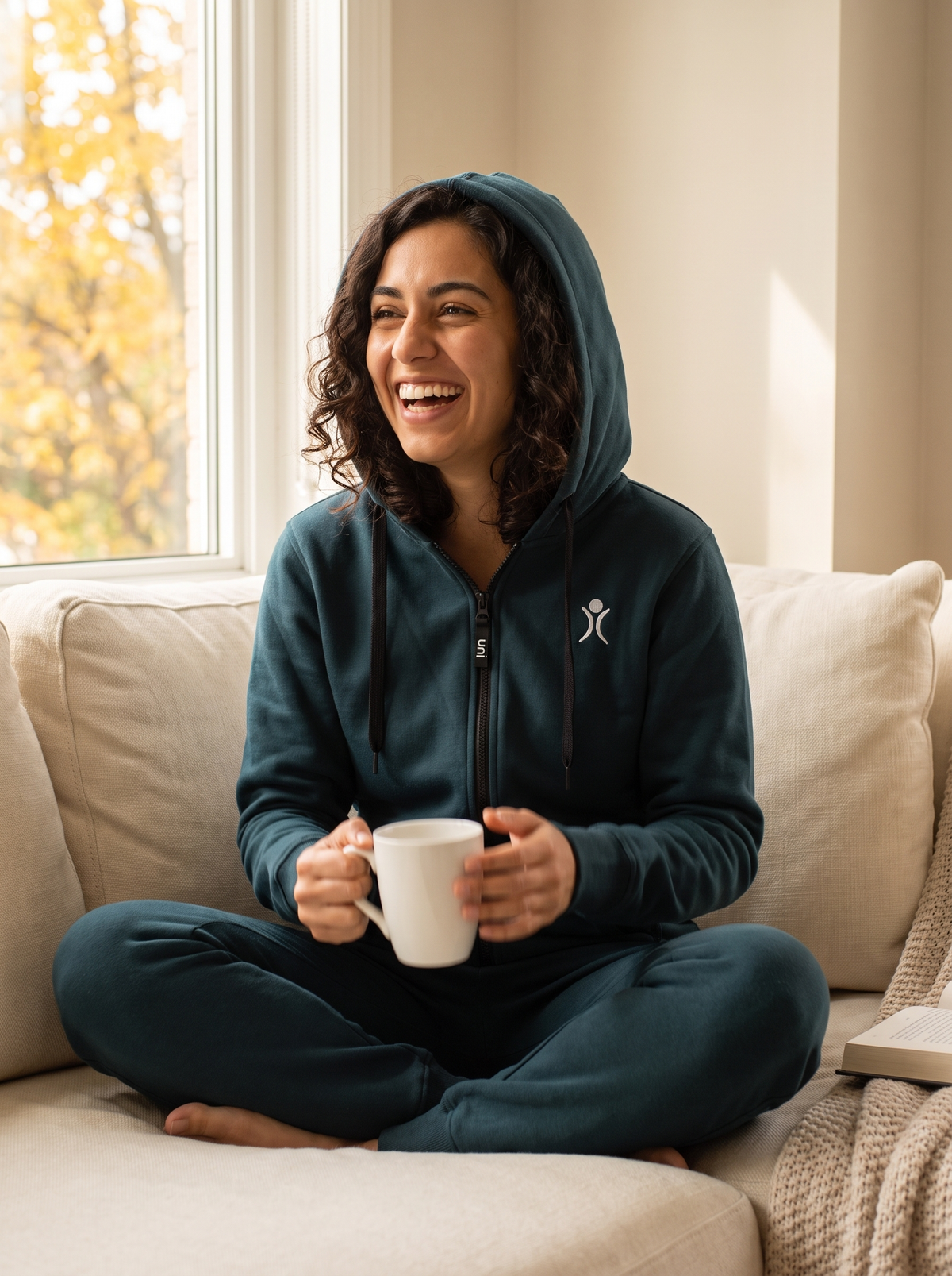 Transformative Teal onesie, woman relaxing on a sofa with tea | Unichill adult unisex fleece onesie designed in Calgary